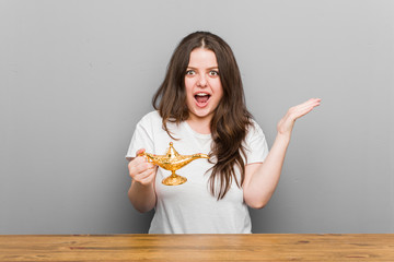 Young plus size curvy woman holding a magic lamp celebrating a victory or success