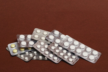 A set of blisters with pills one on top of the other, on a brown background.  