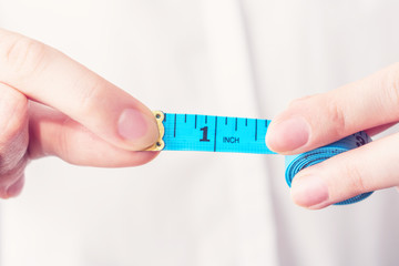 Girl with tape measure shows 1 inch length, female hand, close up, cropped image, toned