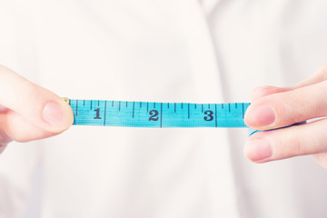 Girl with measuring tape shows 3 inch length, female hand, close up, cropped image, toned