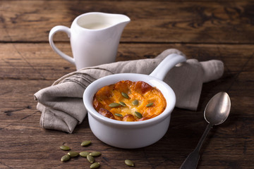 Pumpkin cheese casserole in ceramic mold with pumpkin seeds and cream over wooden texture background