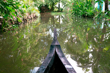 Fototapeta na wymiar riding wood fishing boat in kerala backwaters village water channel under palm trees, a pristine natural environment during monsoon season