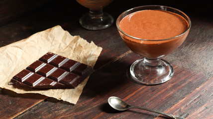 A bowl with chocolate mousse, dark chocolate and a teaspoon on the old dark brown table background