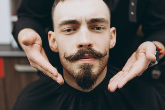 stylish attractive man with a beard in a barbershop. Shaving and modeling a contemporary beard shape in retro style, the barber shaves his client