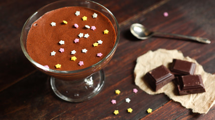 Bowl with chocolate mousse decorated with multi-colored sugar stars, three pieces of dark chocolate...