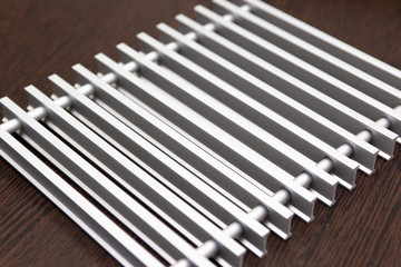 On a dark table lies a lattice of silver metal strips connected by inserts.