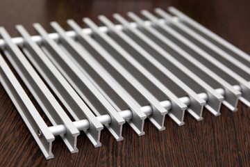 On a dark table lies a lattice of silver metal strips connected by inserts.