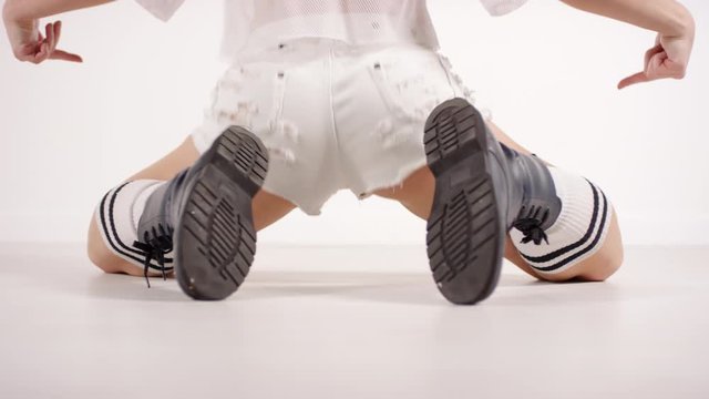 Low section rear view shot of sexy female dancer in distressed shorts and grunge boots performing twerk on her knees in studio