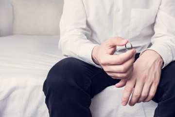 Fototapeta na wymiar Concept of divorce and family disintegration. Man with wedding ring sitting in a marital bedroom, close up, cropped image, toned