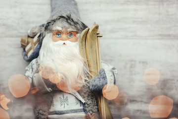 Beautiful santa claus in glasses with skis and gifts on wooden background. Blurred yellow lights on the Santa.