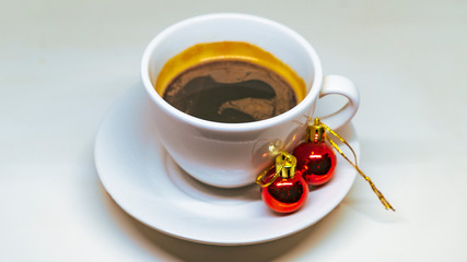 White hot cup of coffee with two christmas tree toys and tinsel. Concept of christmas drink on a white background.