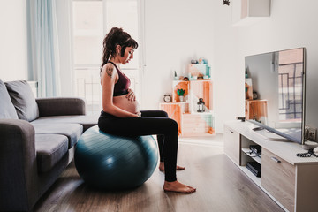 young pregnant woman at home sitting on pilates ball, healthy lifestyle