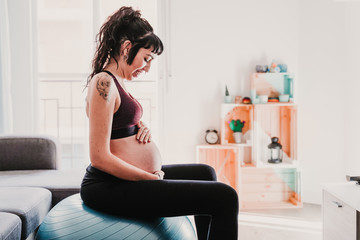 young pregnant woman at home sitting on pilates ball, healthy lifestyle