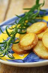 Slices of fried potatoes and fresh rosemary on vintage plate
