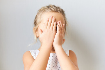 Shy timid little girl covering face, feeling scared. Embarrassed female kid posing isolated with...