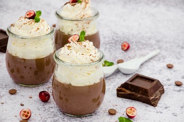 Chocolate cream (pudding, jelly, panna cotta) on agar agar with whipped cream on top in glass jars on a light stone background.