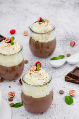 Chocolate cream (pudding, jelly, panna cotta) on agar agar with whipped cream on top in glass jars on a light stone background.