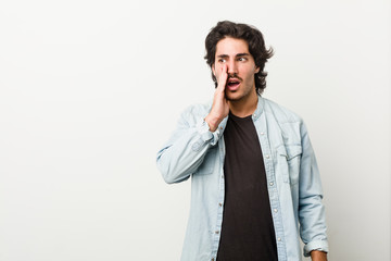 Young handsome man against a white background is saying a secret hot braking news and looking aside