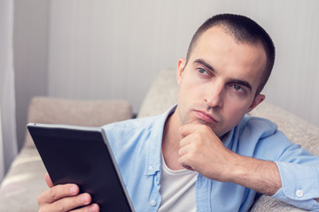 Thoughtful man with e-book sitting at home, portrait, toned