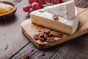 Segment of Brie cheese or soft cow's - French camembert  on wooden board with  grapes, honeycomb and pecan nuts.