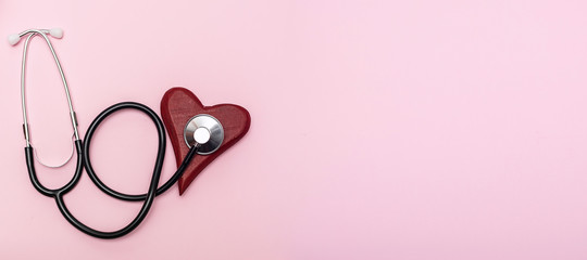 Long wide banner with red wooden heart and medical stethoscope on pink pastel background. Heart...