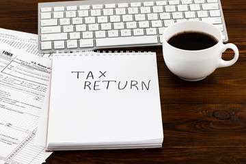 Tax Return written on paper note with tax form, and cup of coffee