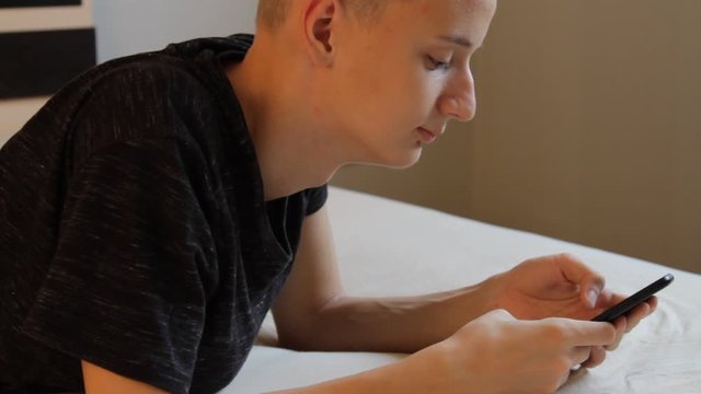Close-up portrait of young teenager boy texting messages and playng a game using his phone