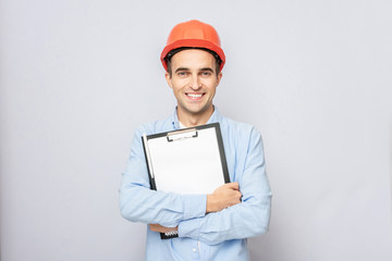 Builder in hardhat with building plans, man smiling, grey background, copy space