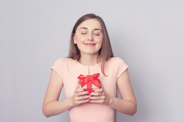 Beautiful woman received a gift. The girl is happy and closed her eyes with pleasure. Portrait, grey background, copy space, toned