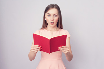 Stunned girl reads a book, her mouth open in surprise, grey background, toned