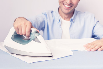 Concept of chores. Man ironing clean shirt, husband happy to do housework, cropped image, toned