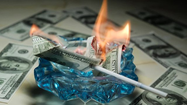 Money burns in an ashtray next to a smoldering cigarette. The concept of high costs of smoking