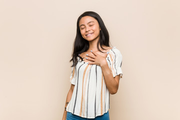 Young cute chinese teenager Young blonde woman wearing a coat against a pink background laughs out loudly keeping hand on chest.