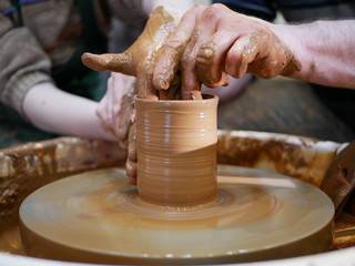 The master Potter teaches the child to make a clay jug on a modern Potter's wheel with an electric drive. The hands of a child and an adult man are stained with clay. Teaching pottery.