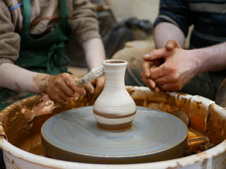 Fototapeta na wymiar The master Potter helps the child to paint a clay jug with white paint on a modern Potter's wheel with an electric drive. Drawing a pattern on a ceramic vase.