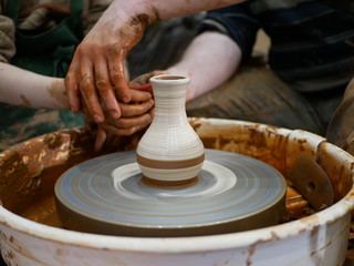 The master Potter helps the child to paint a clay jug with white paint on a modern Potter's wheel with an electric drive. Drawing a pattern on a ceramic vase.