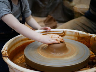 Fototapeta premium The master Potter teaches the child to make a clay jug on a modern Potter's wheel with an electric drive. The hands of a child and an adult man are stained with clay. Teaching pottery.