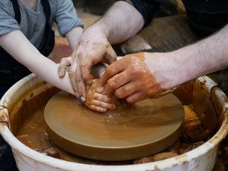 The master Potter teaches the child to make a clay jug on a modern Potter's wheel with an electric drive. The hands of a child and an adult man are stained with clay. Teaching pottery.