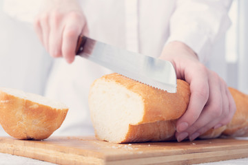 Person with knife, bread on the kitchen table, closeup, toned