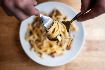 High angle closeup shot of a person reeling up the pasta with a spoon and a fork
