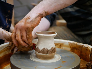 The master Potter helps the child to paint a clay jug with white paint on a modern Potter's wheel with an electric drive. Drawing a pattern on a ceramic vase.