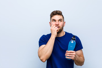 Young caucasian sportsman holding an isotonic drink relaxed thinking about something looking at a copy space.