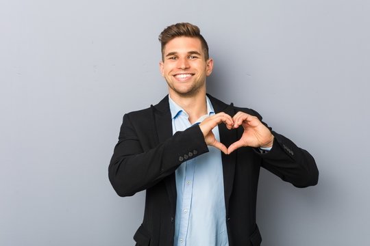Young handsome caucasian man smiling and showing a heart shape with hands.