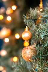 Golden balls and bokeh lights on a green Christmas tree, winter background for greeting card, atmosphere of cosiness and celebration