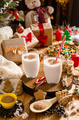 Christmas and New Year eggnog drink in glass cups on a wooden stand on the table with gifts, Christmas cookies, candles, sweets