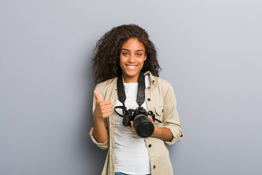 Young african american photographer woman holding a camera smiling and raising thumb up