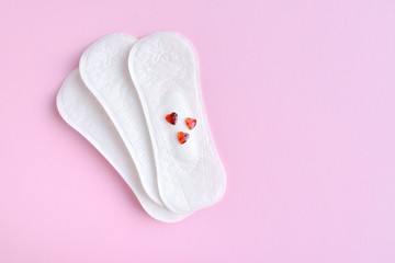 Daily soft cotton pads with red decorative hearts on pink background with empty space for text. Menstrual pad. Women's health concept monthly period days. Woman critical days, menstruation cycle 