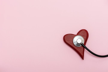 Flat lay overhead of red wooden heart and medical stethoscope on pink pastel background with copy space for your text. Heart diseases prophylaxis and diagnostic concept. Health care concept.