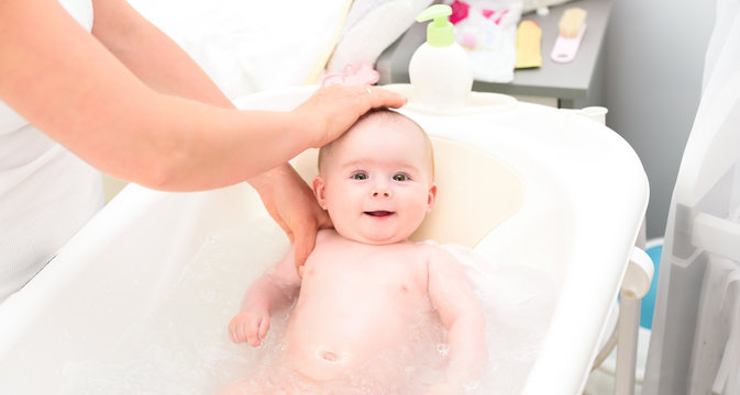 Adorable baby girl in bath with mother. Looking up with big brown eyes and smiling. Copy space