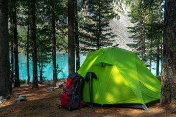 Camping site in the woods by the lake, green tent and backpack.